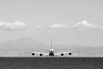 Airplane on runway by sea against sky