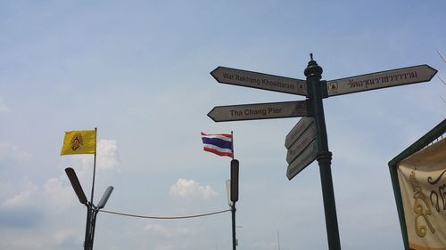 Low angle view of directional sign and thai flag against sky