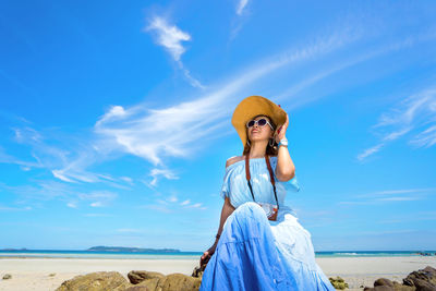 Woman wearing sunglasses at beach against blue sky