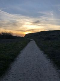 Road amidst field against sky during sunset