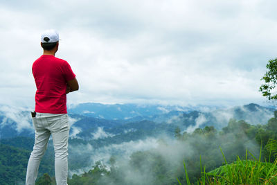 Rear view of man standing on mountain against sky