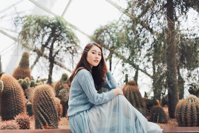 Portrait of young woman sitting on plant against trees