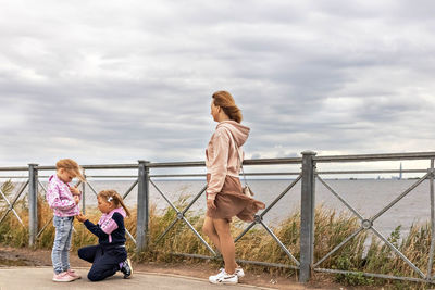 Rear view of women standing on railing against cloudy sky