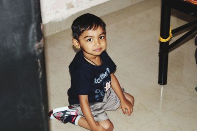 High angle portrait of cute boy sitting on tiled floor