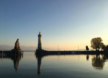 Reflection of lighthouse and statue on lake during sunset