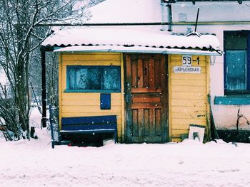 Snow covered house by building during winter