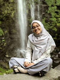 Portrait of smiling young woman sitting against waterfall