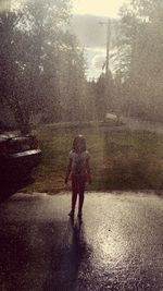 Rear view of woman walking on wet road