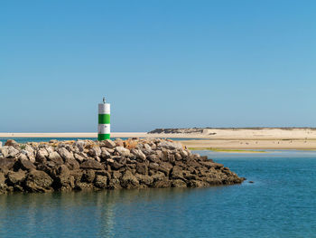 Lighthouse by sea against clear blue sky