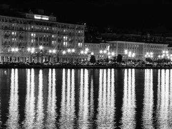 Illuminated buildings by river against sky at night