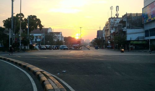 City street by buildings against sky during sunset