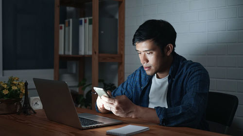 Young woman using mobile phone while sitting on table