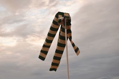 Low angle view of windsock on pole against cloudy sky