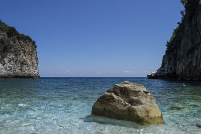 Rock formation by sea against clear blue sky