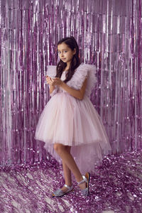Beautiful girl with big eyes in a pink dress stands against the background of new year's tinsel