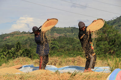 Women standing on field by trees against sky