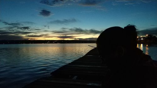 Silhouette woman looking at lake against sky during sunset