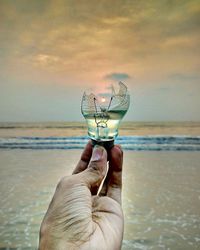 Cropped hand of man holding broken light bulb at beach