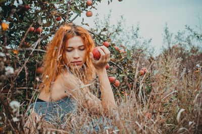 Side view of woman with apple sitting amidst plants on field