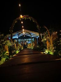 Illuminated footpath amidst buildings against sky at night