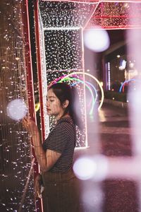 Woman standing amidst illuminated lights at night