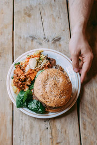 Cropped hand holding food in plate on wooden table