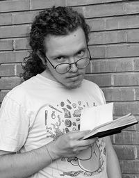 Young man holding a sketchbook while standing against brick wall