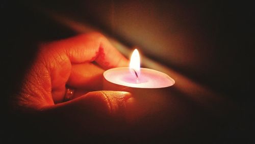 Close-up of hand holding illuminated candle