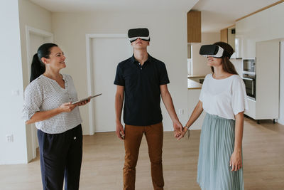 Smiling couple wearing virtual reality simulators while standing by real estate agent on floor