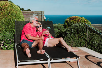 High angle of relaxed senior couple lying on loungers on terrace and drinking refreshing tropical cocktails while enjoying summer holiday