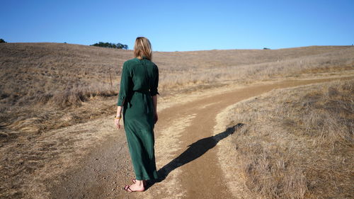 Rear view of woman standing on dirt road against sky