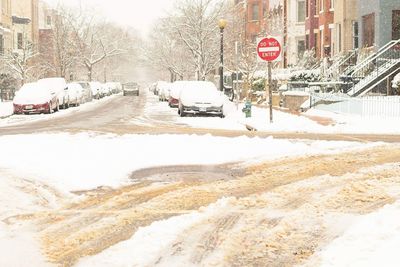 Snow covered road by city during winter