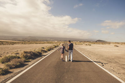 Rear view of couple walking on desert road against sky