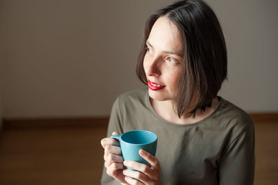Thoughtful woman holding coffee cup at home