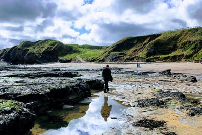 Man standing on rock by river against sky