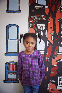 Portrait of cute girl standing against painted wall in kindergarten