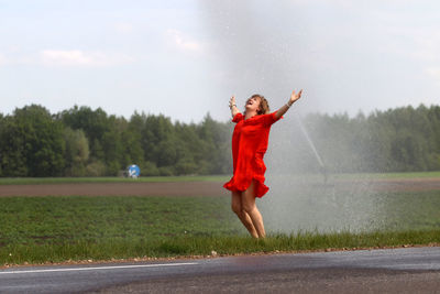 Full length of woman jumping while standing by sprinkler on field