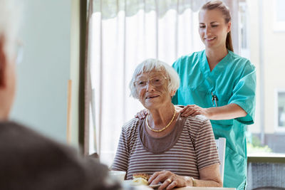 Smiling female caretaker massaging shoulders of senior woman at home