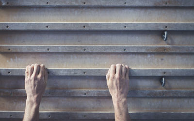 Cropped hands of young man climbing wooden wall