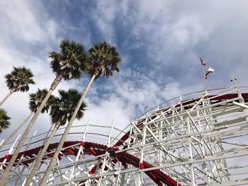 Low angle view of palm trees by rollercoaster against sky