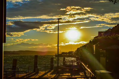 Illuminated city by sea against sky during sunset