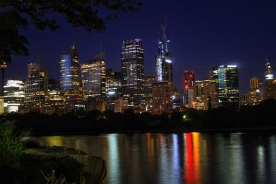 Illuminated buildings by river against sky at night