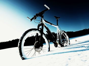 Bicycle on snow covered field against sky