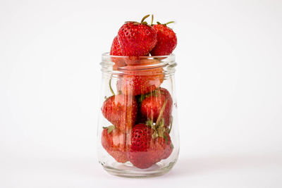 Close-up of strawberries in glass jar against white background