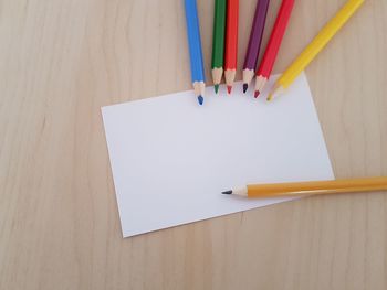 High angle view of colored pencils with blank paper on wooden table