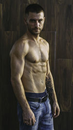 Portrait of shirtless man standing against wall