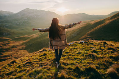 Rear view of woman with arms outstretched on mountain against sky during sunset