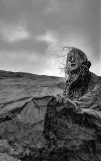 Portrait of young adult feminine boy in poncho against stormy sky