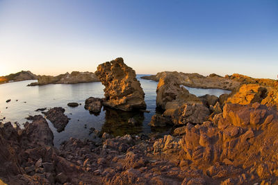 Rock formations on shore against clear sky