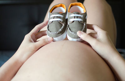 Mid section of pregnant woman holding baby shoes